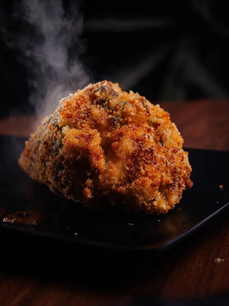 A steaming piece of crispy fried chicken served on a dark plate in a moody setting.