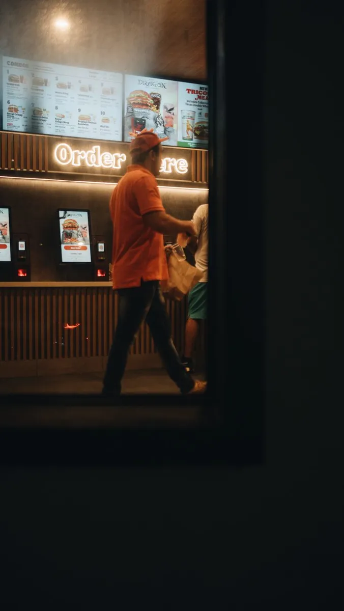 Customers in a fast food outlet using self-service kiosks at night.
