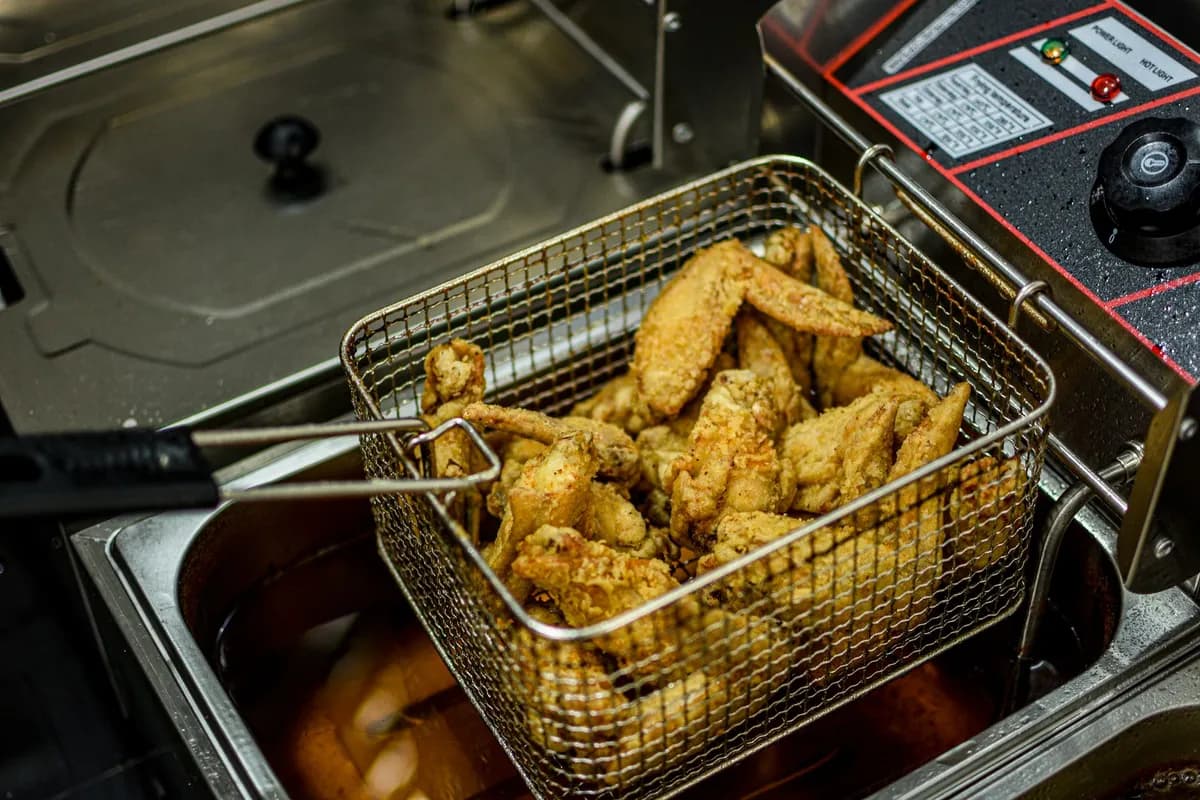Golden brown chicken wings freshly fried in a commercial deep fryer.