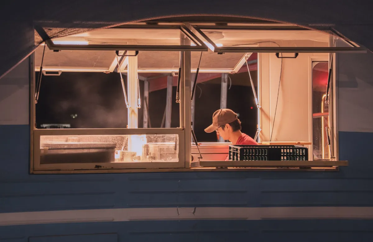A view of a worker inside a food truck at night, captured through an open window.